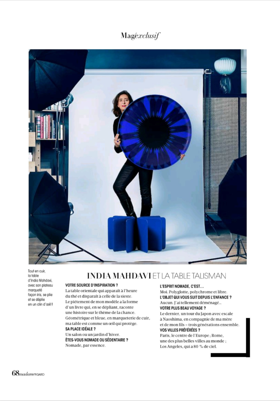 A woman posing in a photography studio, holding a large circular blue and black artwork, surrounded by photography equipment including umbrellas, lights, and a white backdrop.