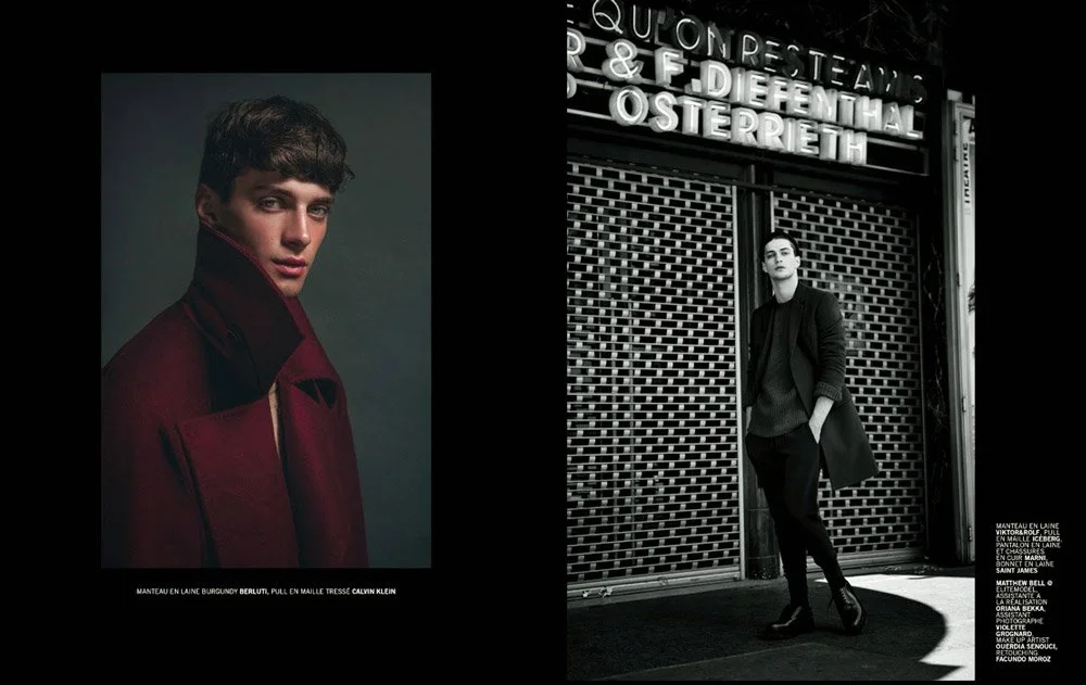 A fashion magazine spread featuring a male model in a red coat on the left page and a male model in a dark outfit standing outside a building with a metal gate on the right page.