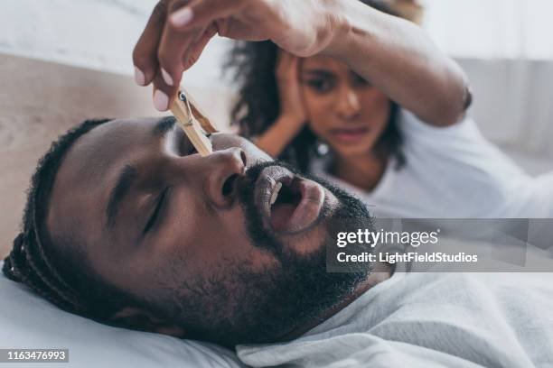 Una donna che si prende cura di un uomo sdraiato a letto, usando un fermaglio per le labbra. La scena rappresenta un momento di attenzione e cura.