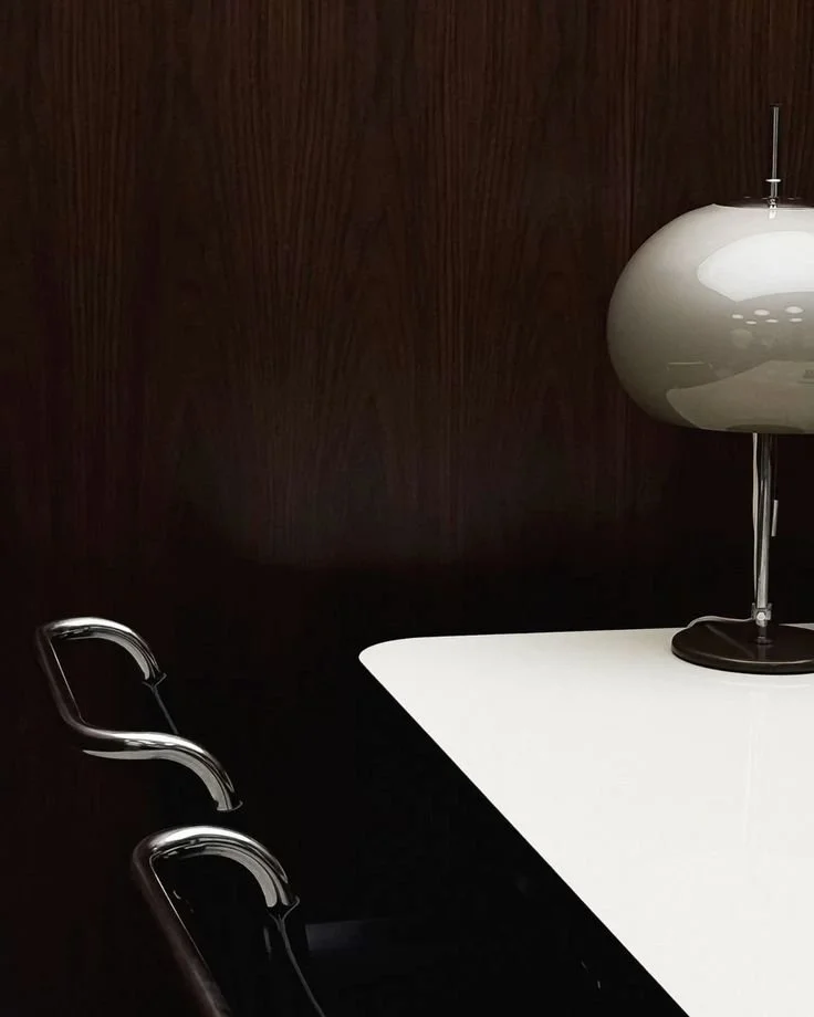 Part of a conference table with a white surface, a modern white oval-shaped lamp, and a dark wooden wall in the background.