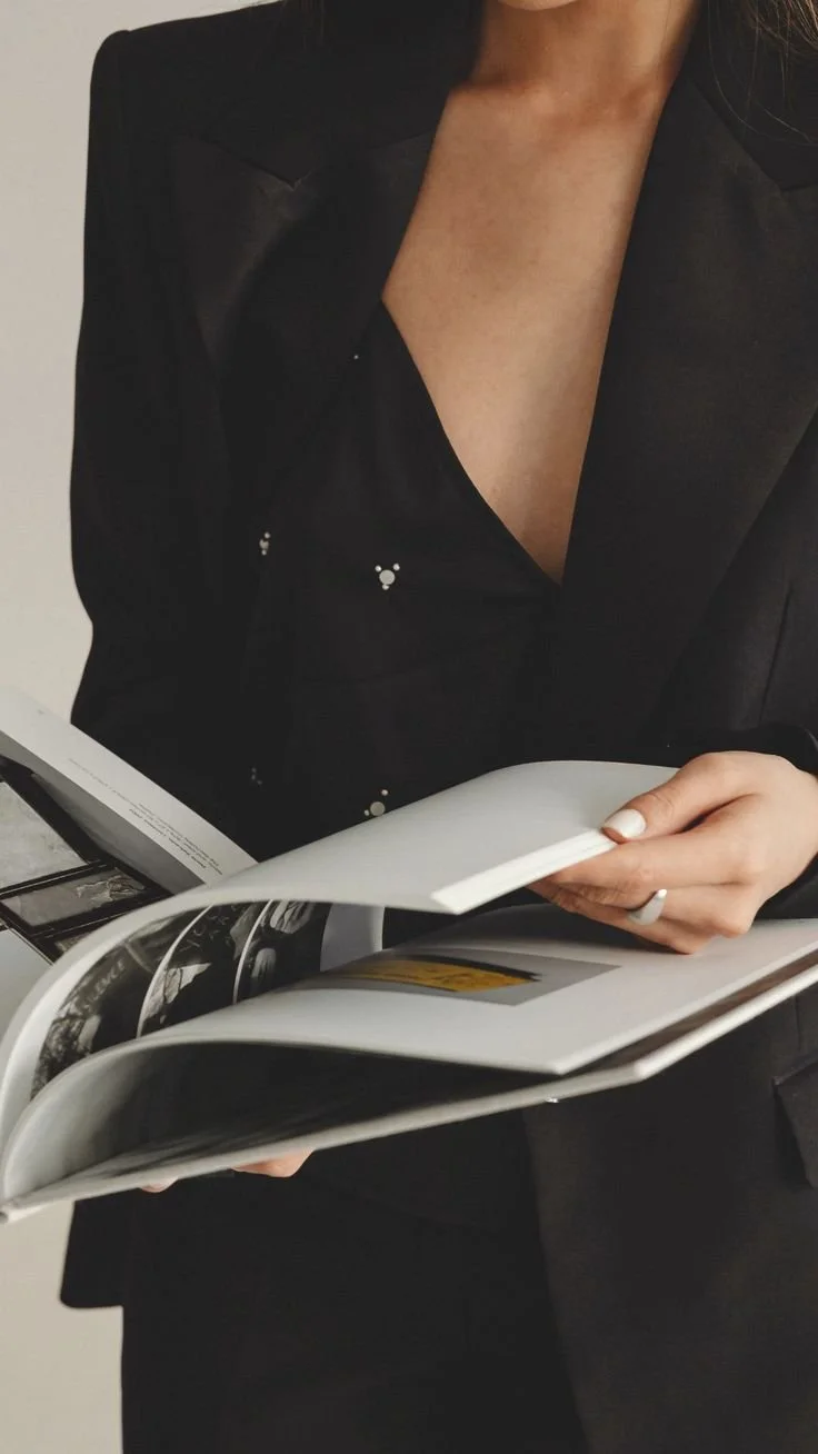 A woman in a black blazer looking at a magazine.