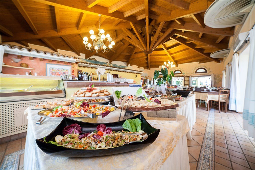 Buffet table with various salads and cold dishes in a restaurant with wooden ceiling and chandeliers.