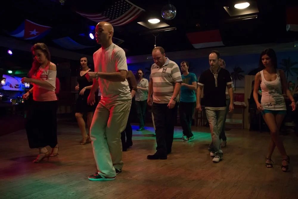 Group of people dancing in a dimly lit room with flags hanging from the ceiling.