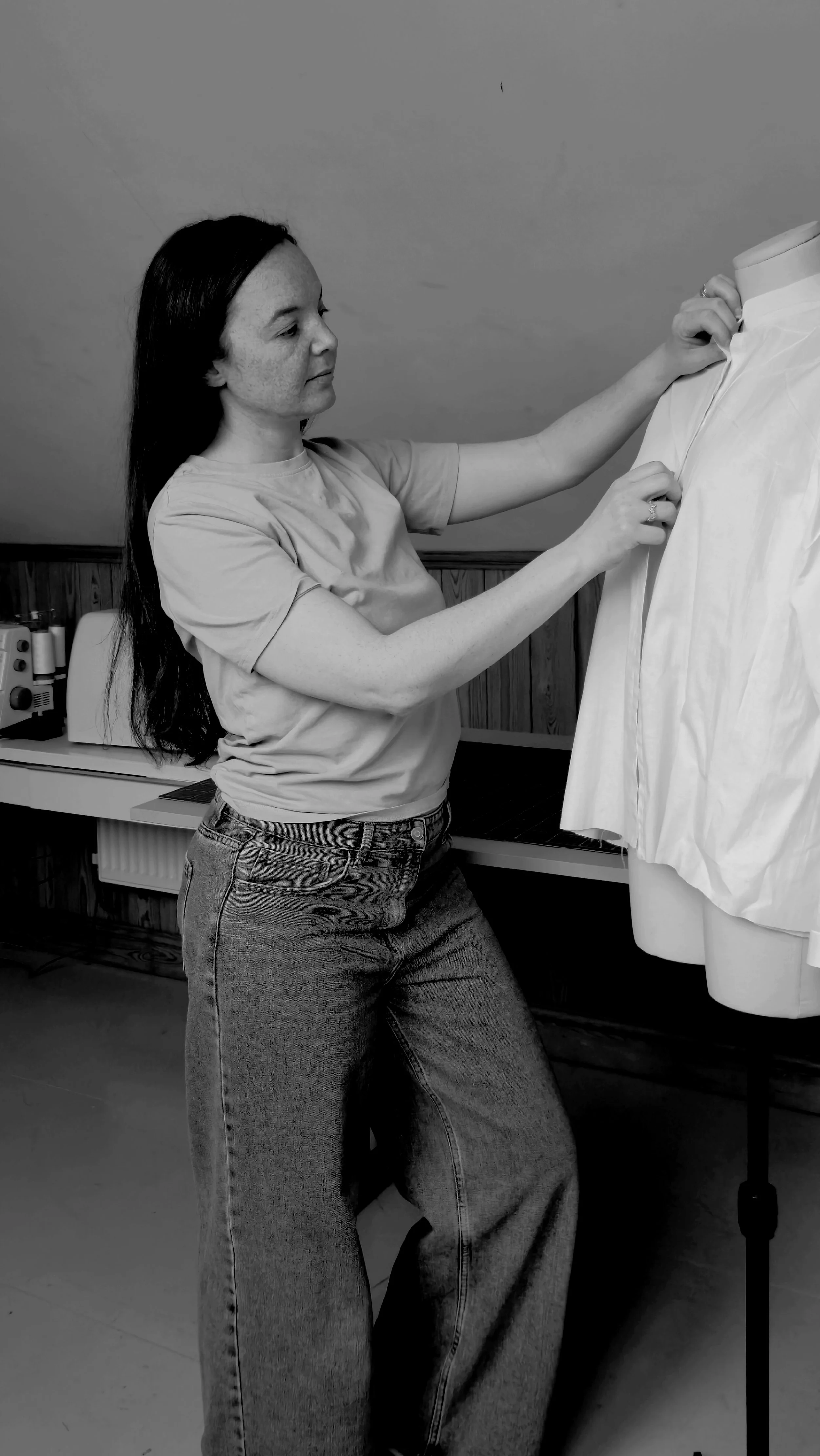 Black & White picture of founder of brand Jess. Adjusting a shirt on a manniquin in her studio
