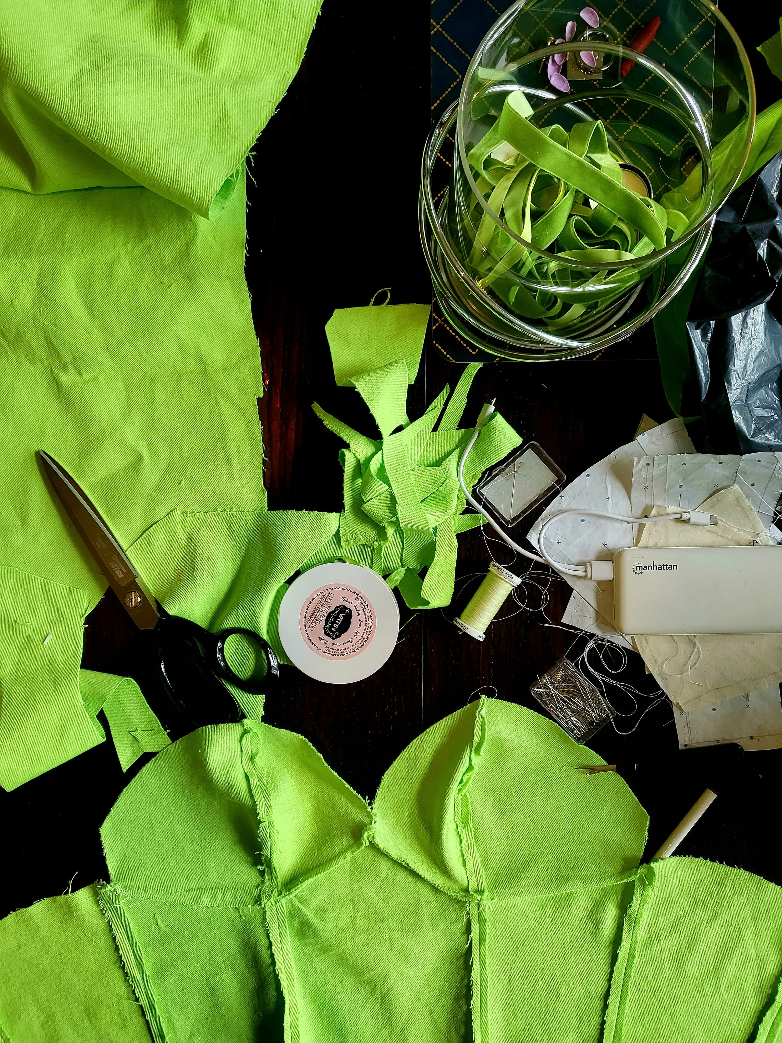 a table with lime green fabric scraps and work in progress of a garment being put together. Also a pair of scissors and needle and thread