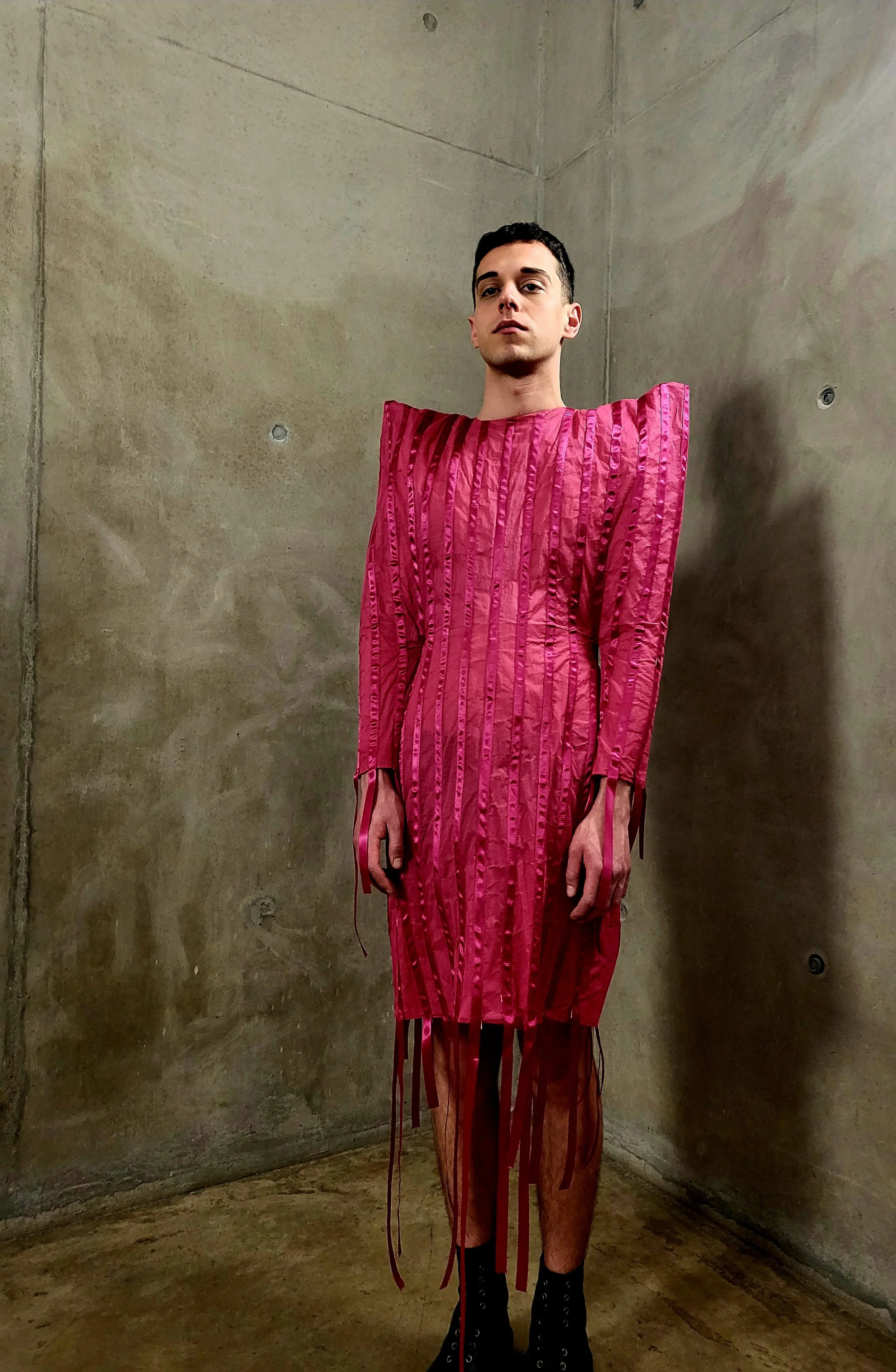 male model in a pink dress, the back drop is a concreate wall