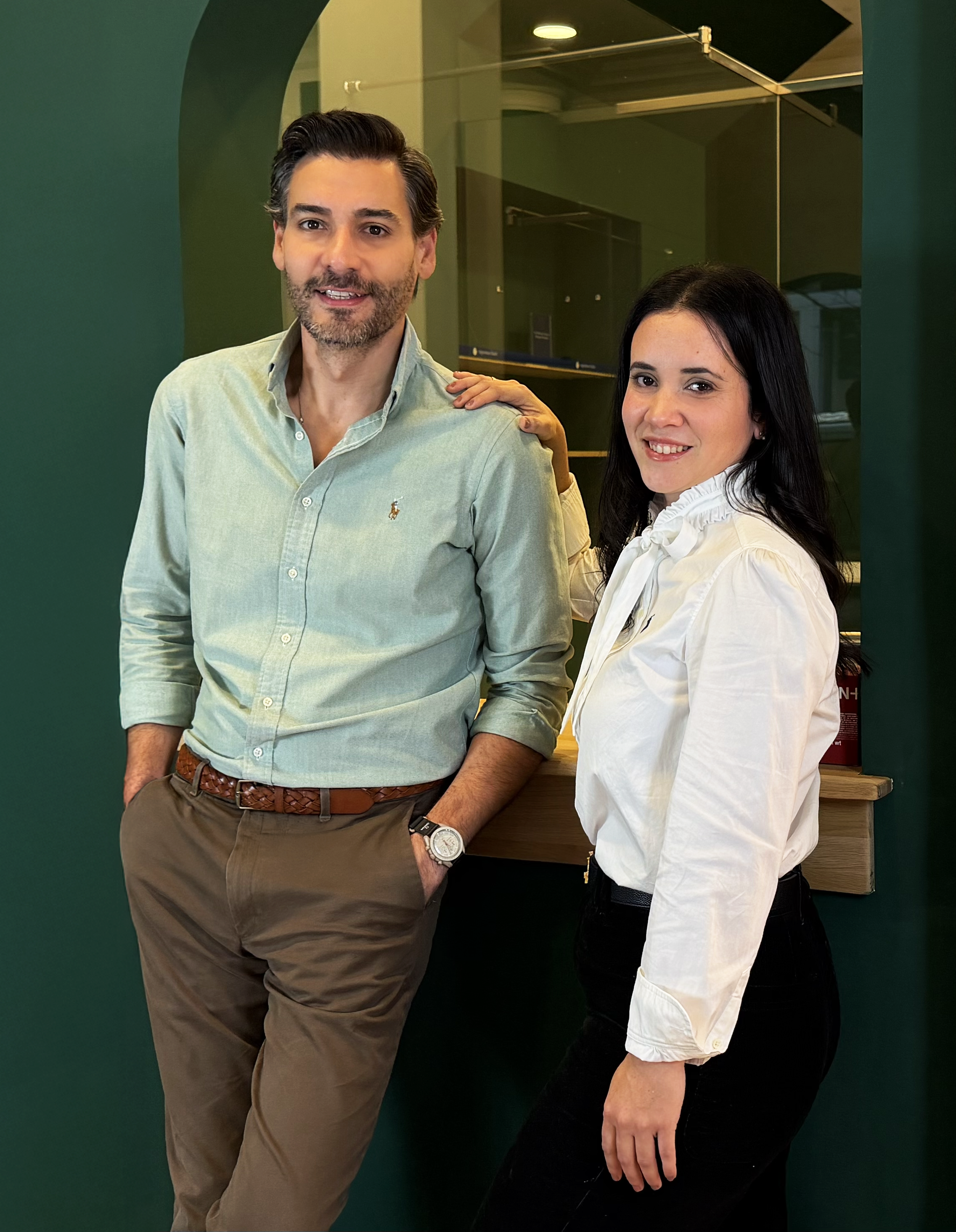 Hombre y mujer posando en un entorno moderno, con paredes verdes y cristaleras.