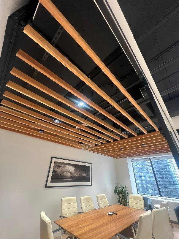 Modern conference room with wooden ceiling slats, a wooden table, white chairs, a framed picture on the wall, a potted plant, and large windows showing a cityscape.