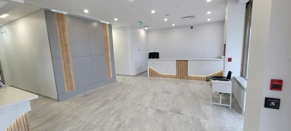 Empty modern reception area with a marble front desk, black chair, and large windows allowing natural light.