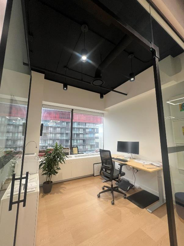 Modern office room with a desk, computer monitor, office chair, large window, potted plant, and glass walls.