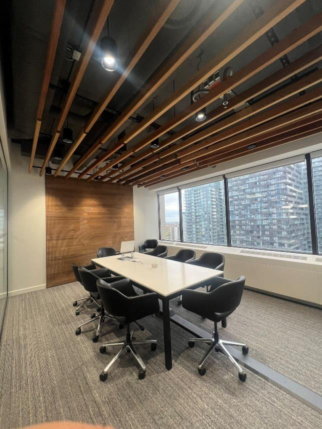 Modern conference room with a white table, eight black swivel chairs, large windows, and wooden ceiling beams.