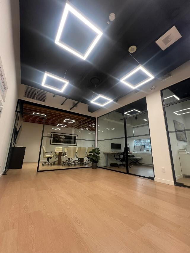 Modern office conference room with beige chairs, conference table, glass walls, potted plant, and unique square LED ceiling lights.