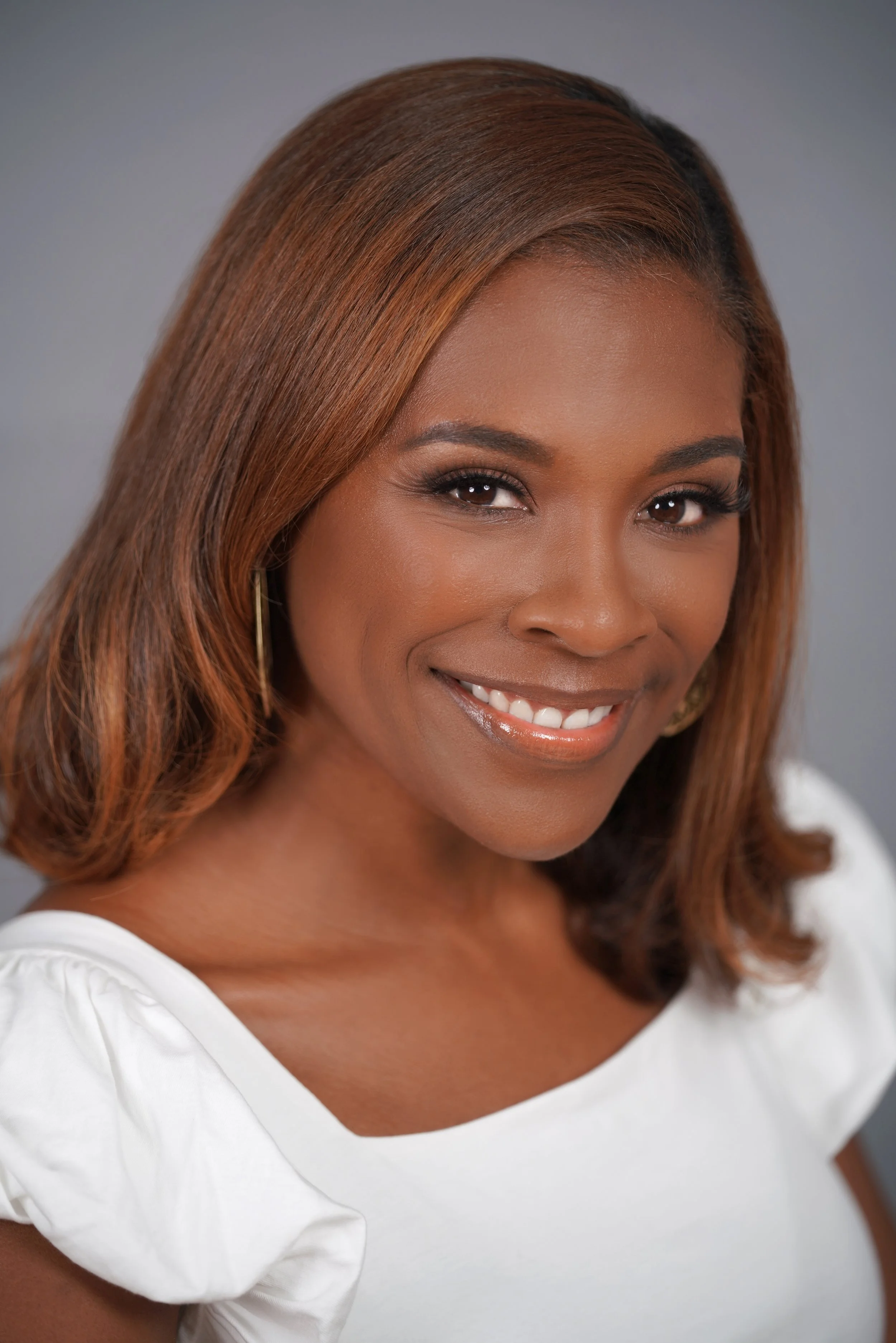 Close-up portrait of an African American woman with shoulder-length brown hair, smiling, wearing a white top and gold earrings.