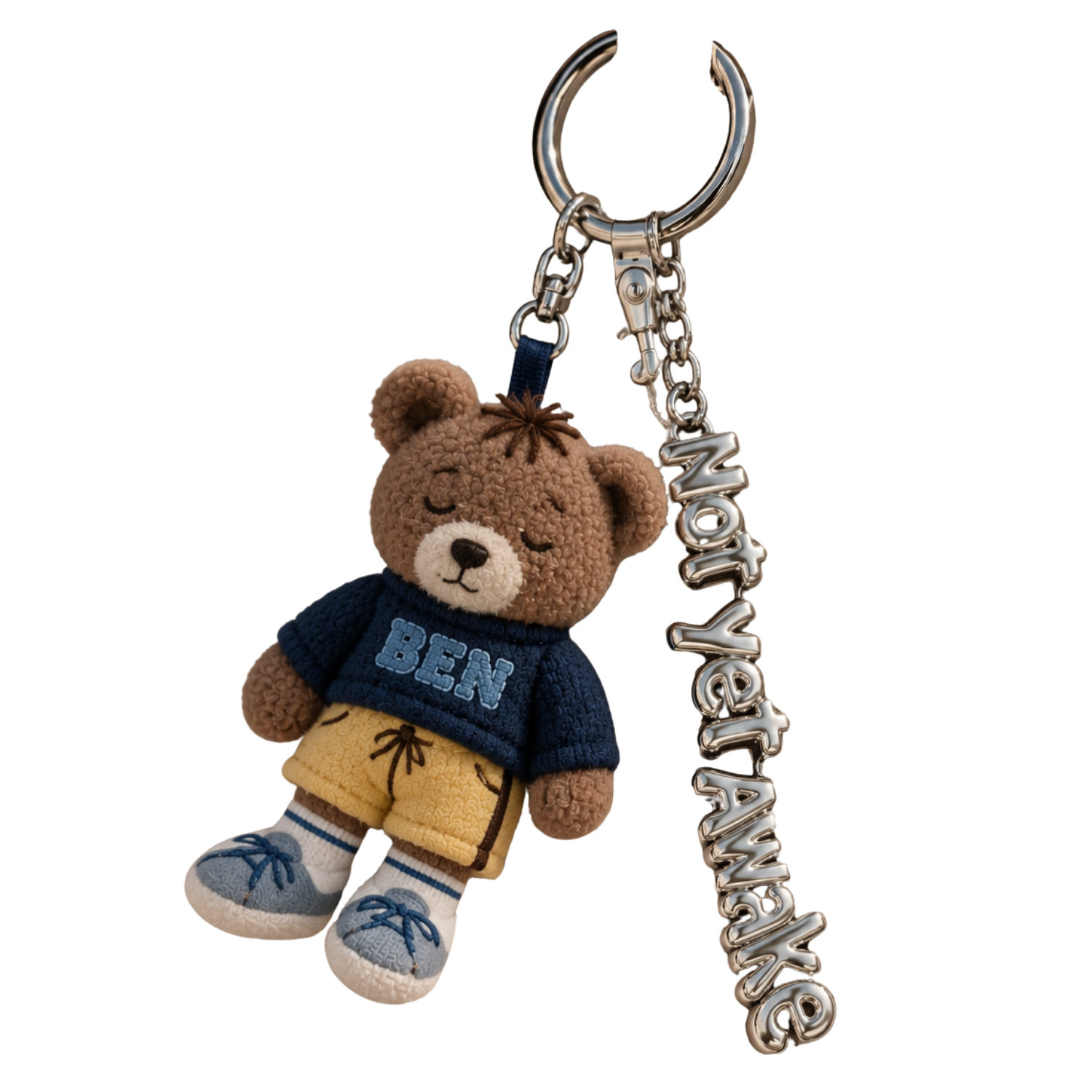 A plush teddy bear keychain wearing a blue sweater with 'BEN' written on it, beige shorts, and blue sneakers, attached to a metal chain with a 'SOMETHING' word charm.