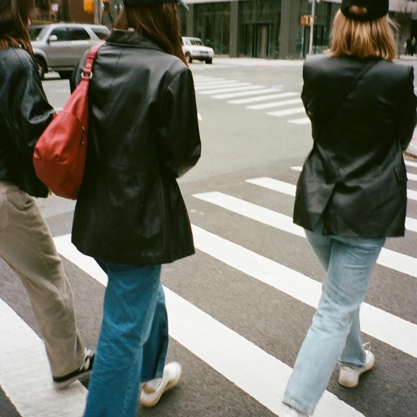 Three women crossing a city street at a crosswalk, dressed in casual clothing with jackets and jeans.