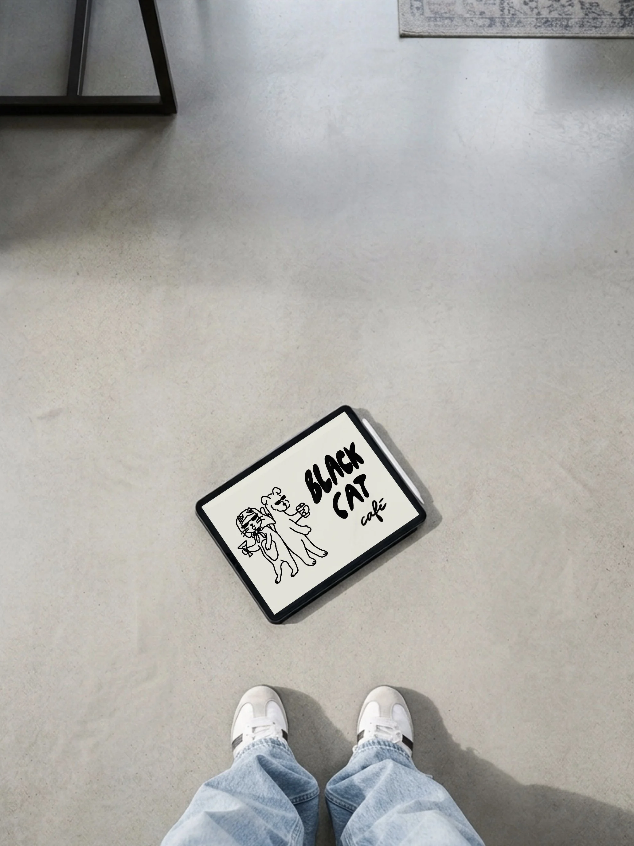 Person wearing white sneakers and blue jeans looking down at a gray floor with a sign that says "Black Cat Cafe" and a cartoon illustration of two cats