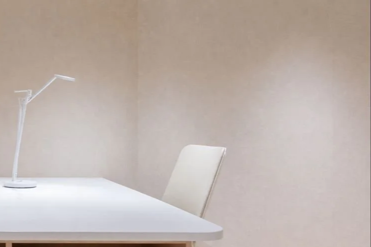 Empty white desk with a modern desk lamp and a white chair in a plain beige room.