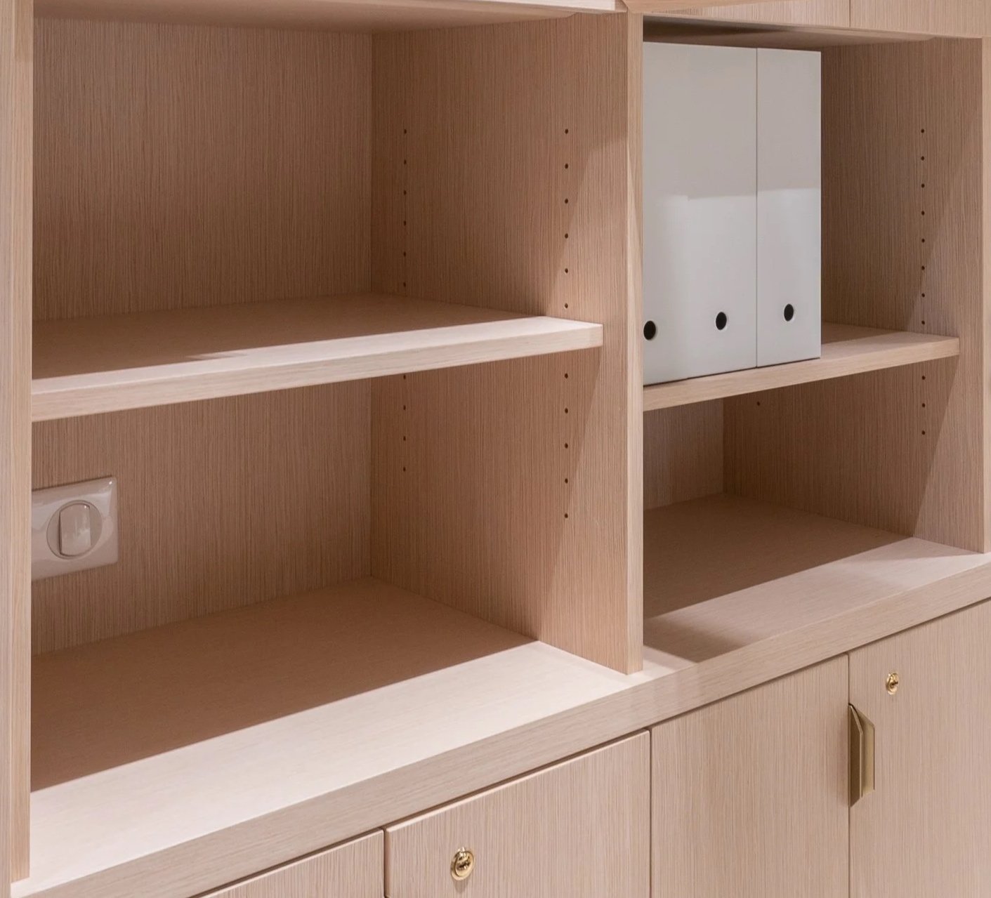 Empty wooden shelving unit with a power outlet on the left side and white binders on the right side.