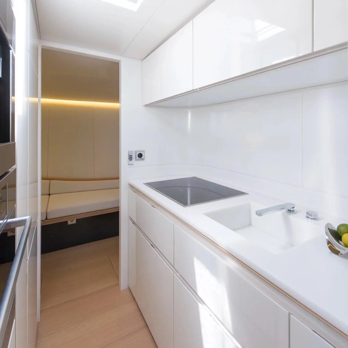 Modern white kitchen with built-in stovetop, sink, and upper cabinets, adjacent to a cozy seating nook with a beige couch and soft lighting.