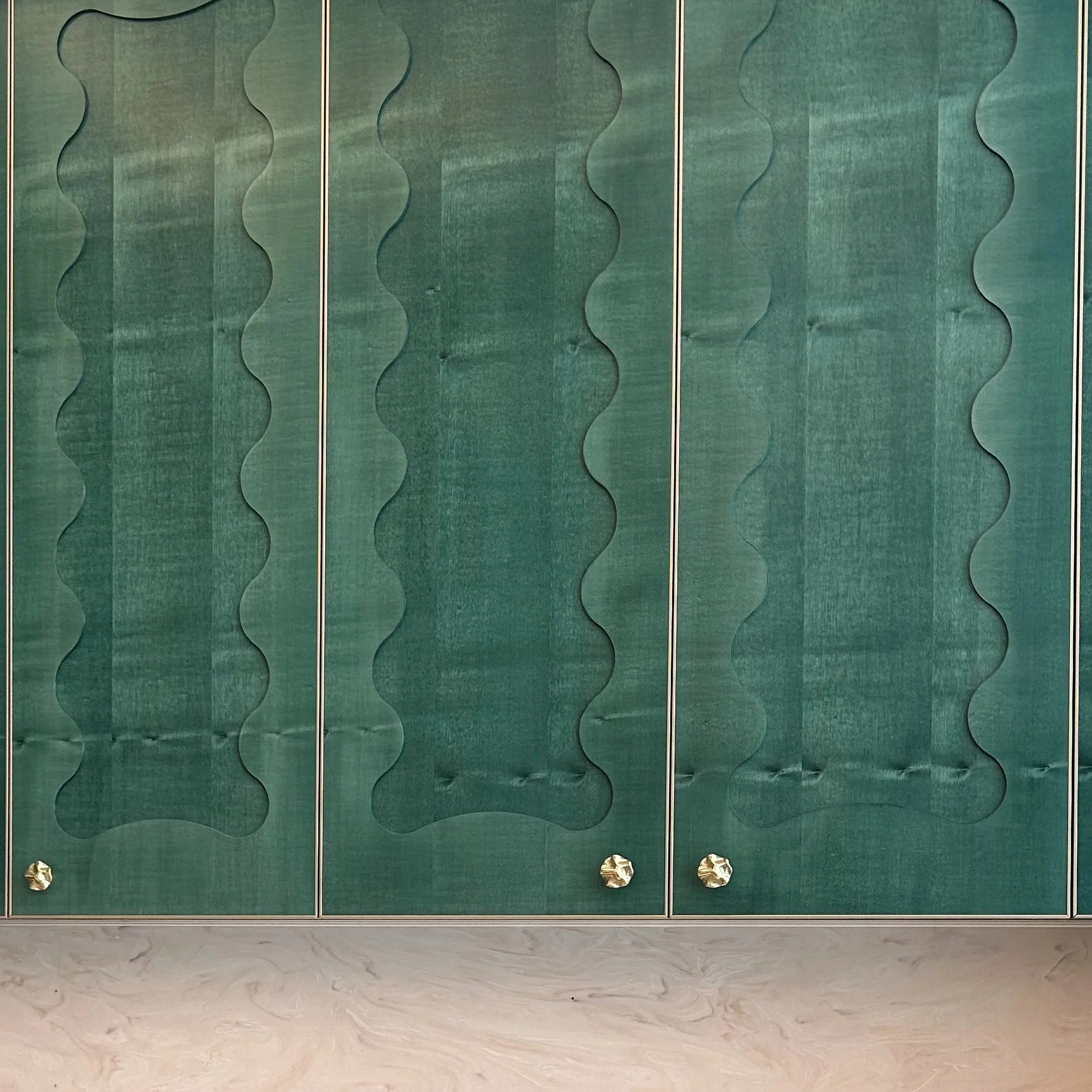 Green textured wall with vertical beige lines and four gold-colored knobs at the bottom.