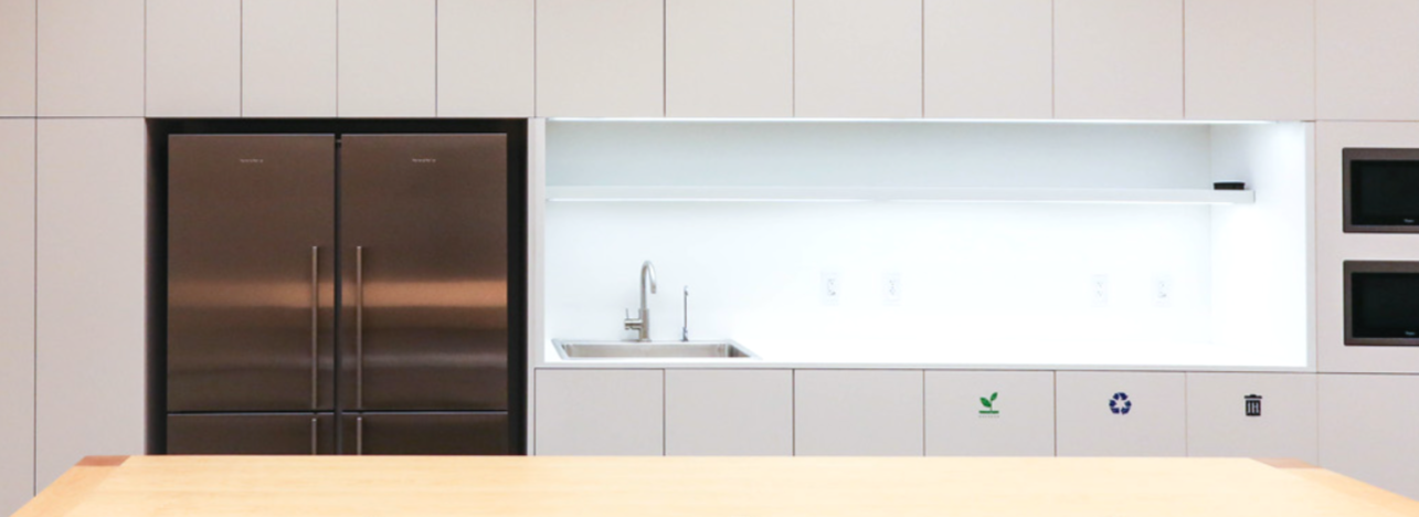 Modern kitchen with stainless steel refrigerator, white cabinets, a small sink, and recycling symbols on the lower cabinets.