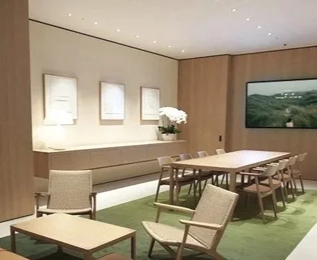 Modern lounge or meeting area with a table and chairs, a sofa, artwork on the wall, and a large landscape painting in the background.