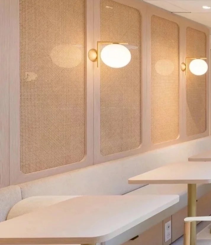 Modern cafe interior with white tables, wooden chairs, wall sconces, and a kitchen area with a counter and plants.