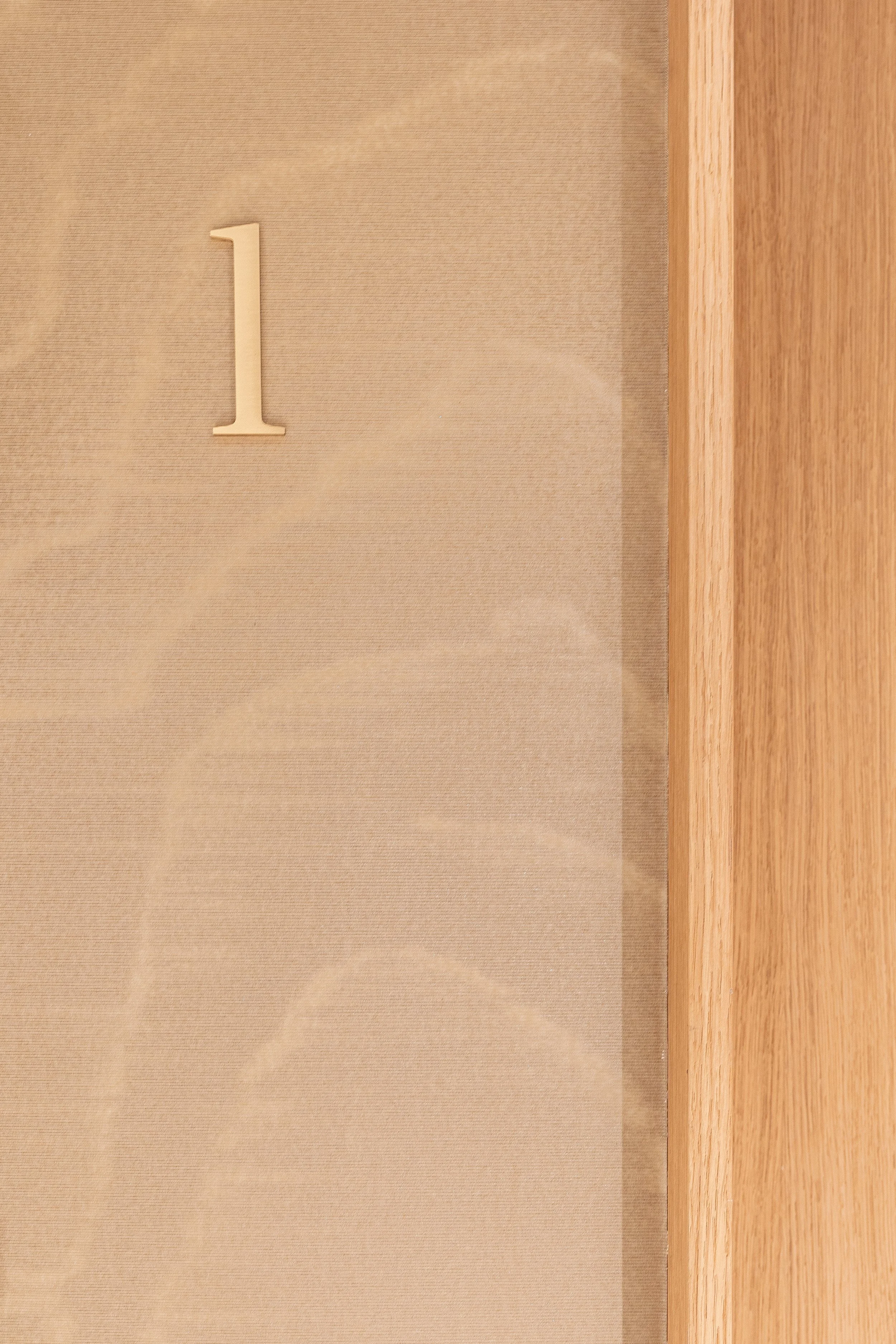 A beige wall with a large number '1' painted or mounted on it, next to a wooden surface or door.
