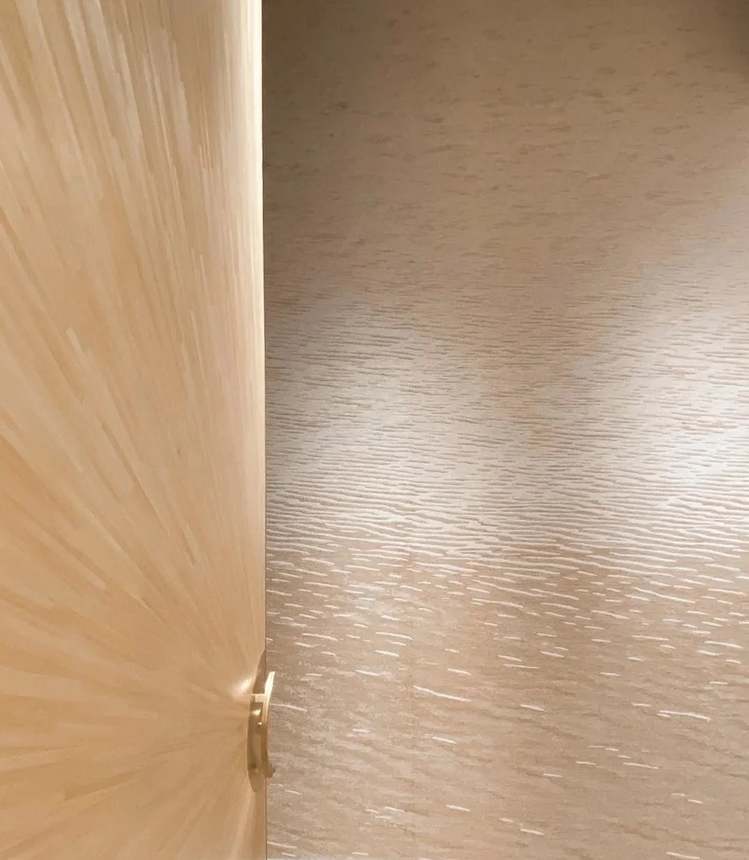 Partially open wooden door with a brass handle, revealing a wood-textured floor.