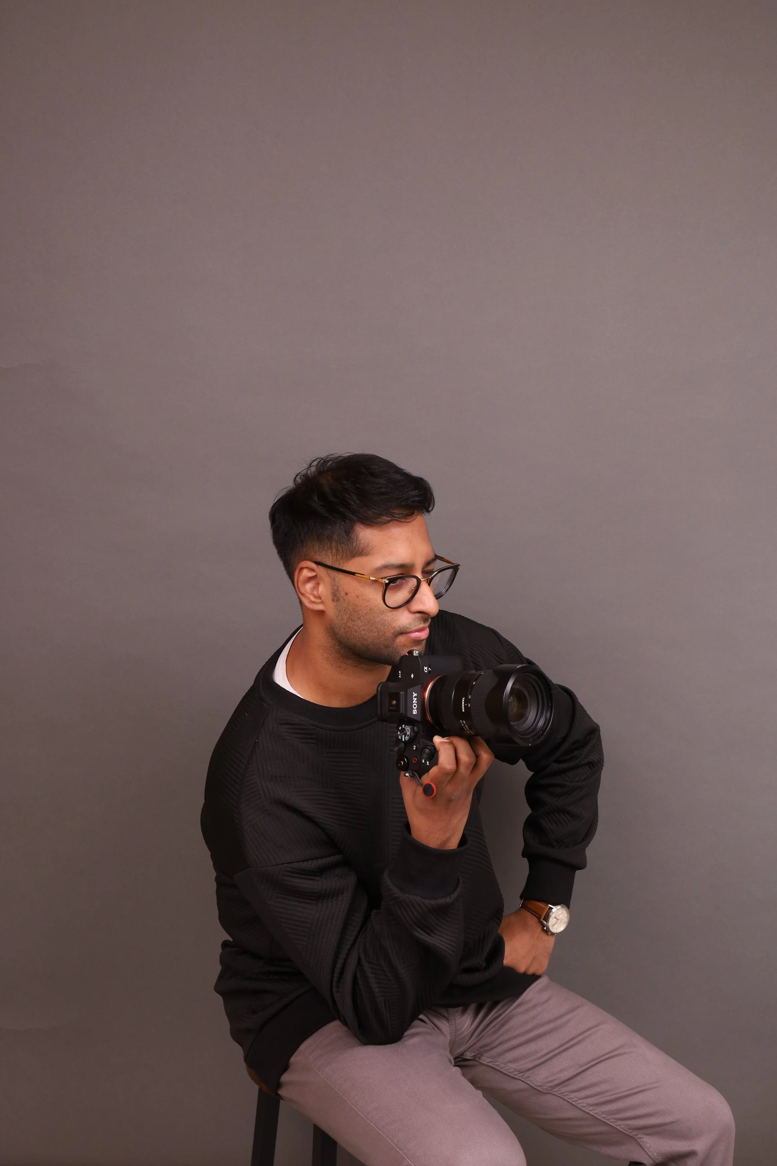 A man with glasses taking photos with a camera against a gray background.