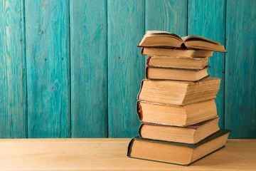 Stack of old books on a wooden surface with a turquoise wooden wall background.