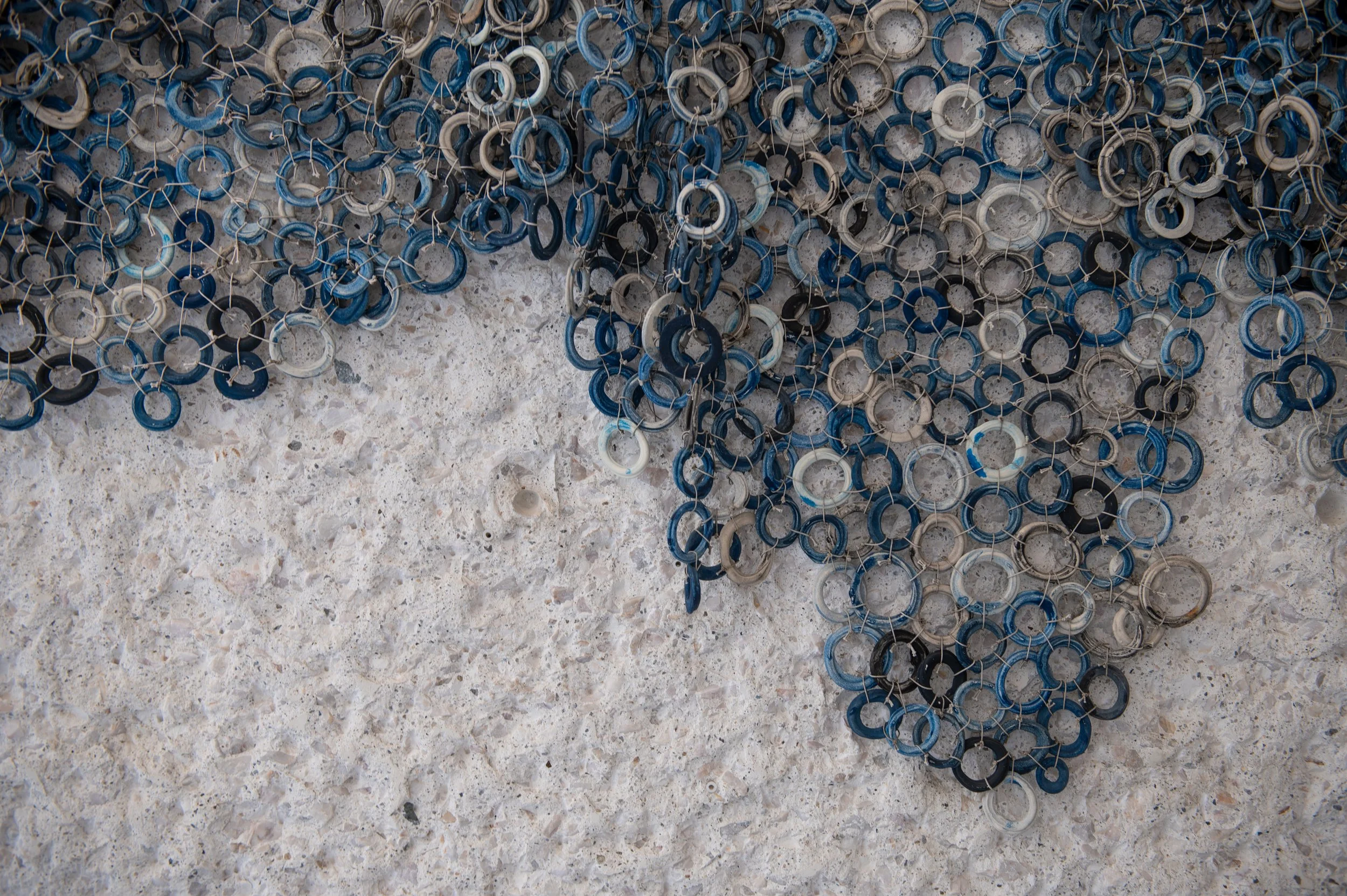 Close-up view of blue and black rubber and white plastic ring keychains hanging on a textured concrete surface.