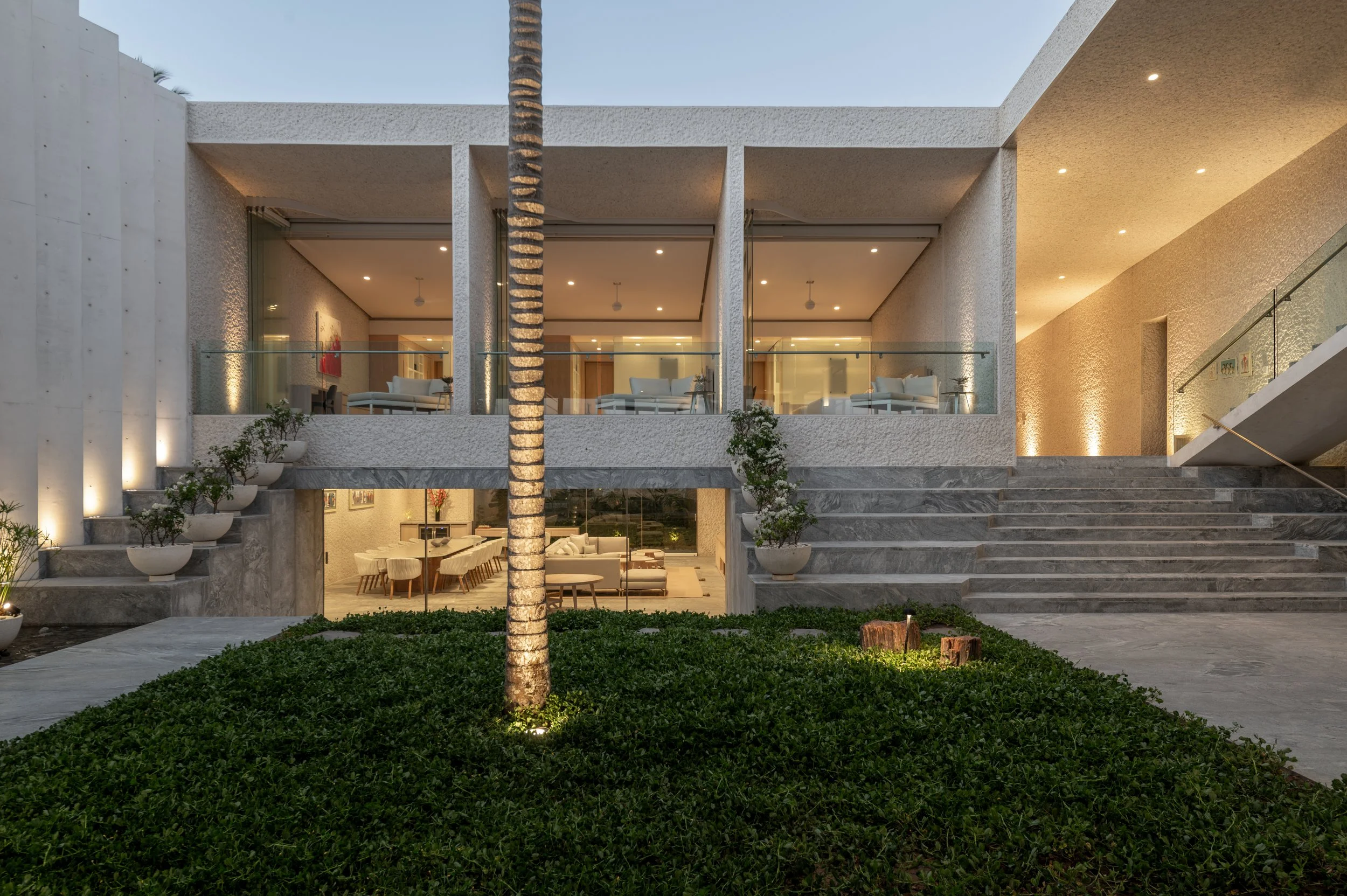 Modern two-story house with a staircase outside, large glass windows, and a wood and concrete exterior, illuminated during evening.