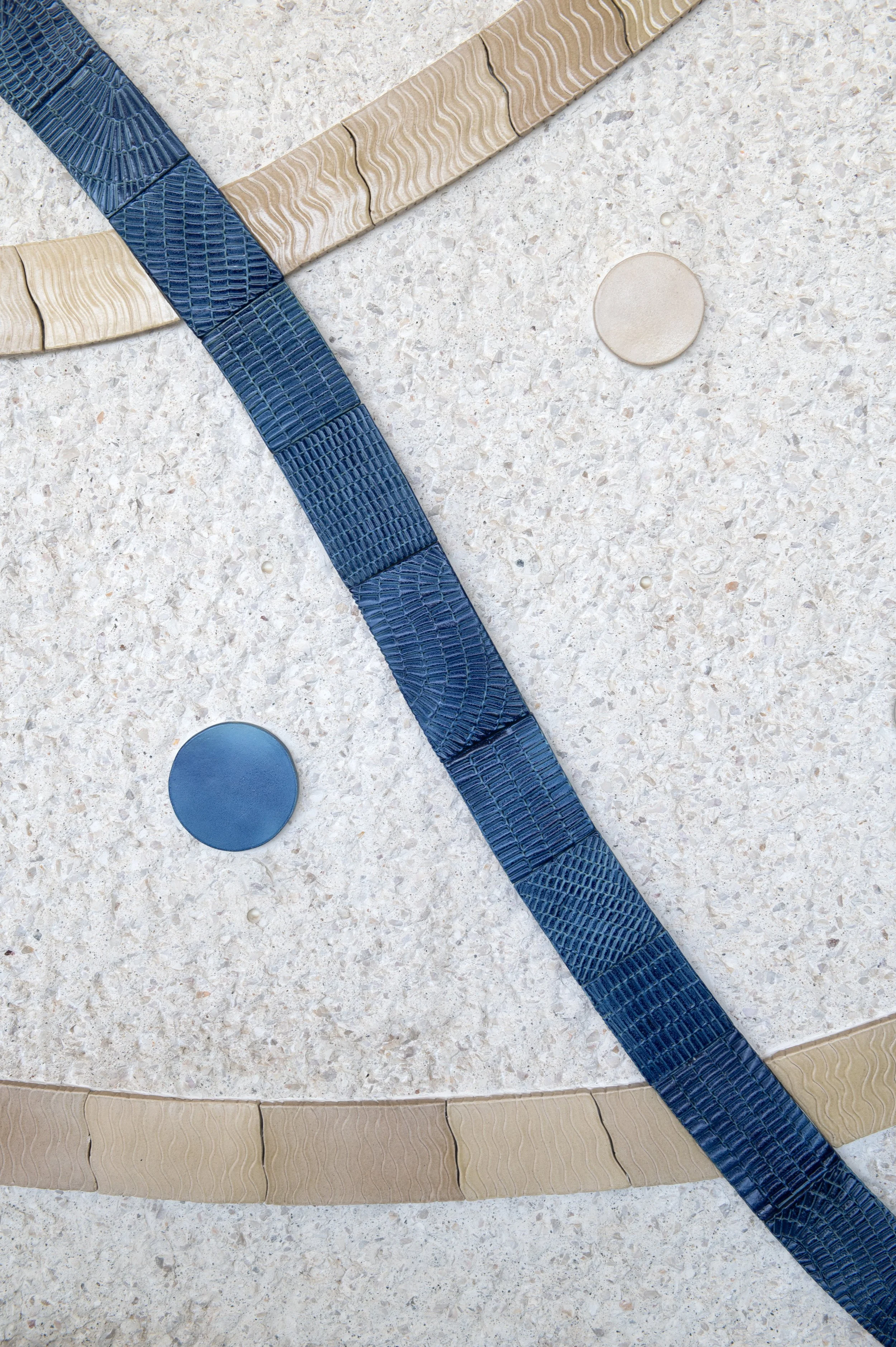 Close-up of decorative building facade with curved stonework, circular tile accents, beige and blue textured tiles, and a terrazzo surface.