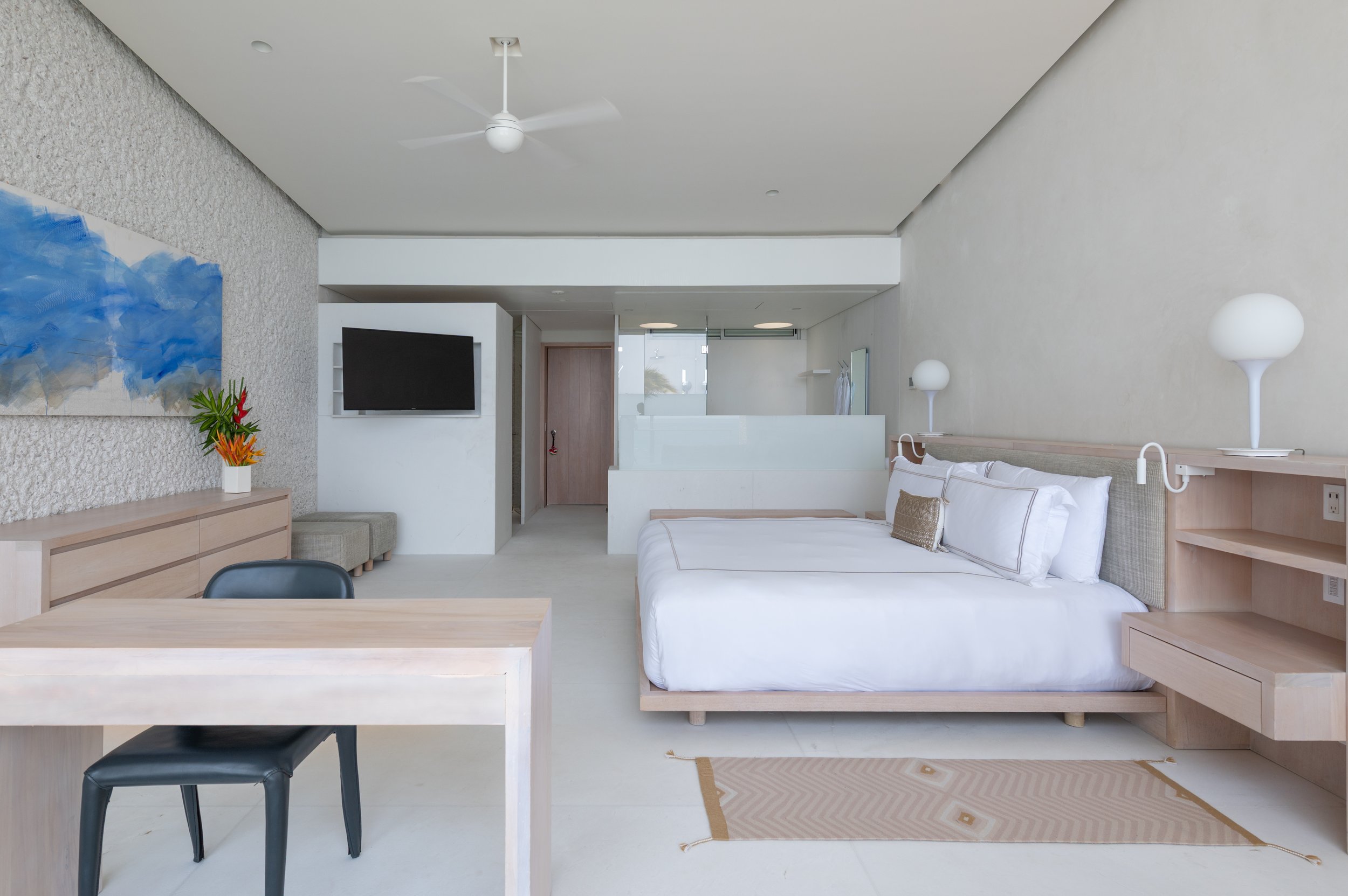 Modern hotel room with a white bed, nightstands with lamps, a flat-screen TV, abstract wall art, and minimal decor.