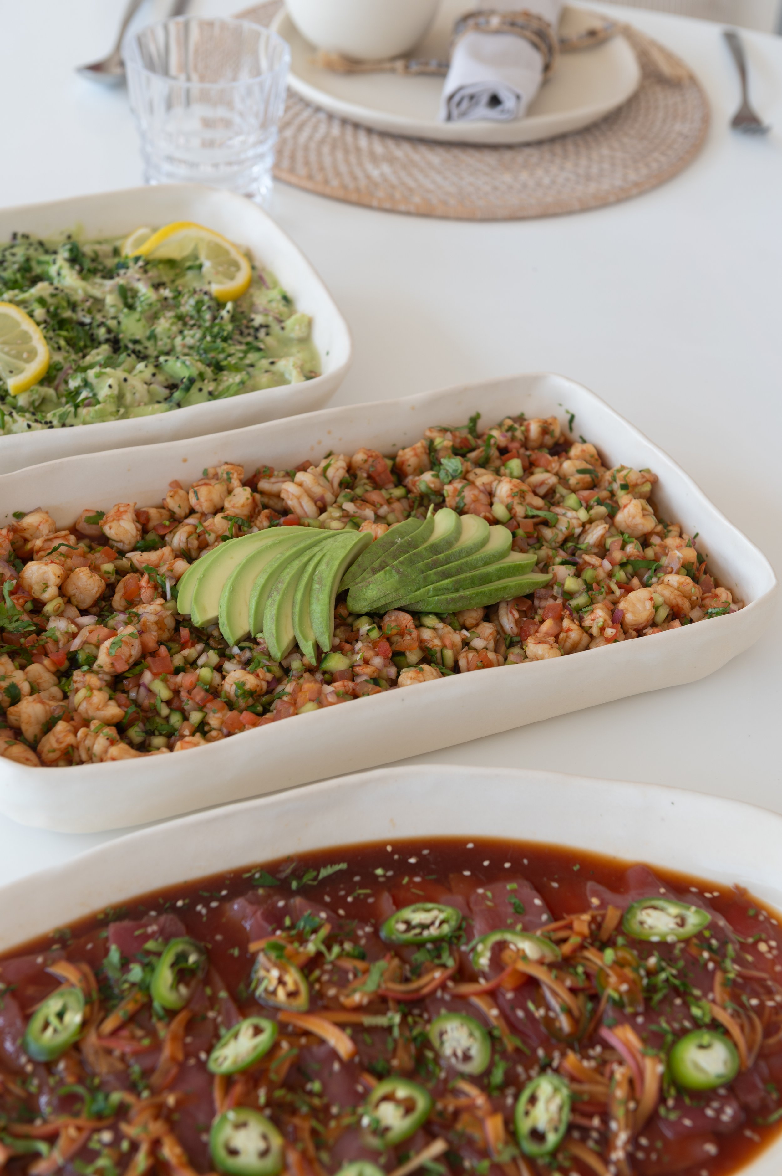 Close-up view of various bowls of Asian-inspired dishes on a table, including a bowl of shrimp salad with avocado and chopped herbs, a bowl of chopped vegetable salad decorated with lemon slices, and a bowl of spicy beef or pork with sliced green chi