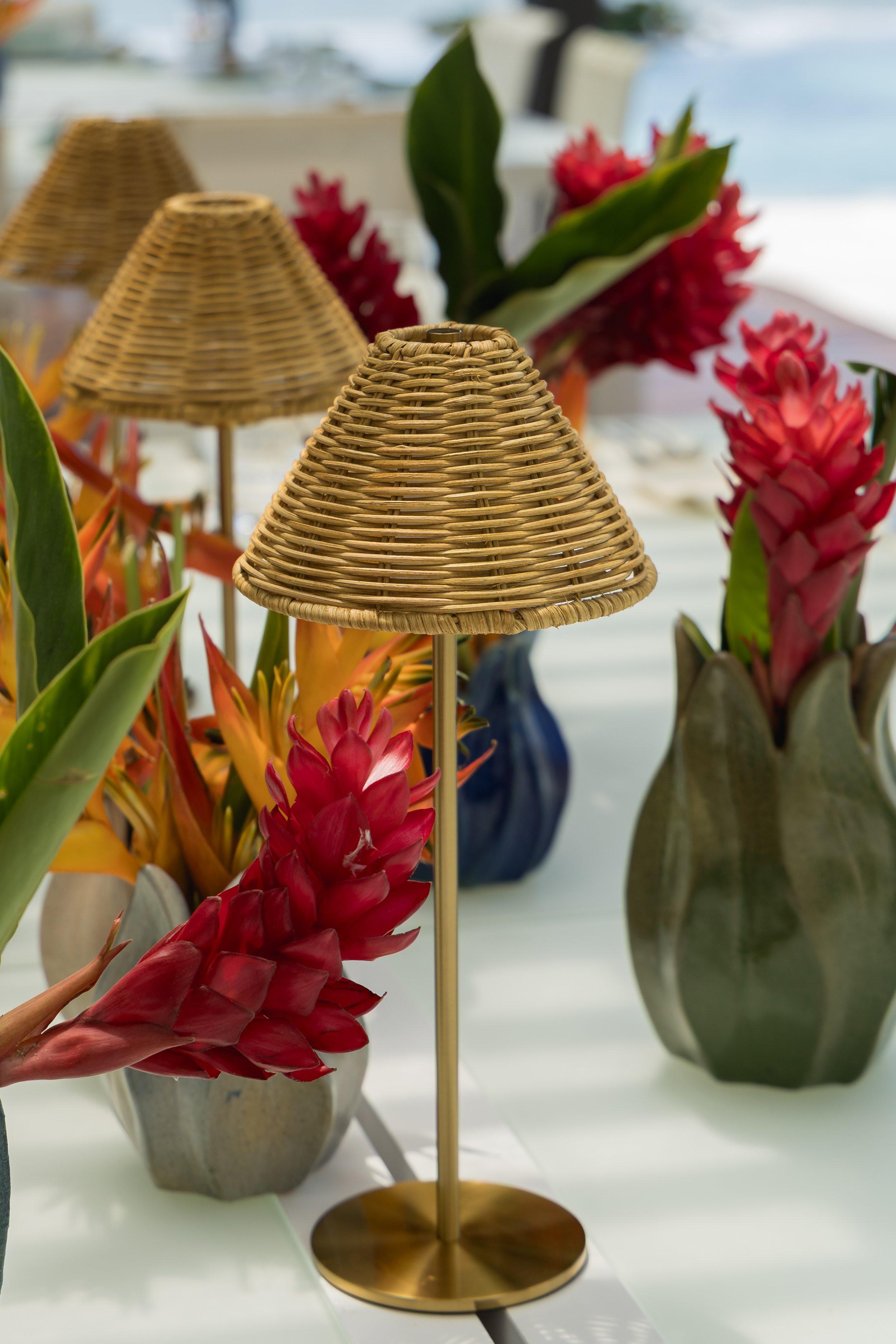 Wicker lamp and colorful tropical flowers in vases on a white table.