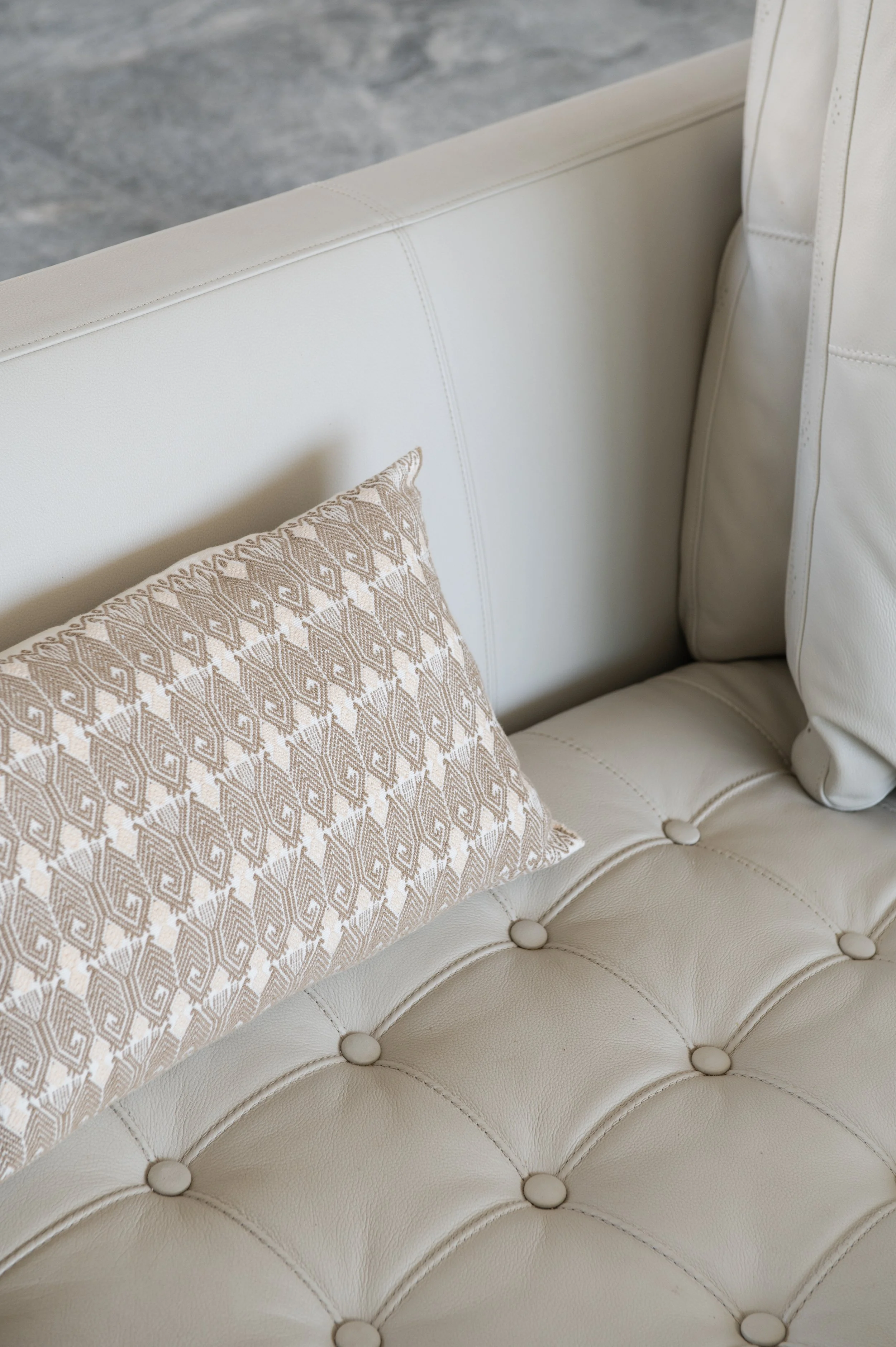 Close-up of a beige tufted leather or faux leather couch with a patterned beige and white pillow.