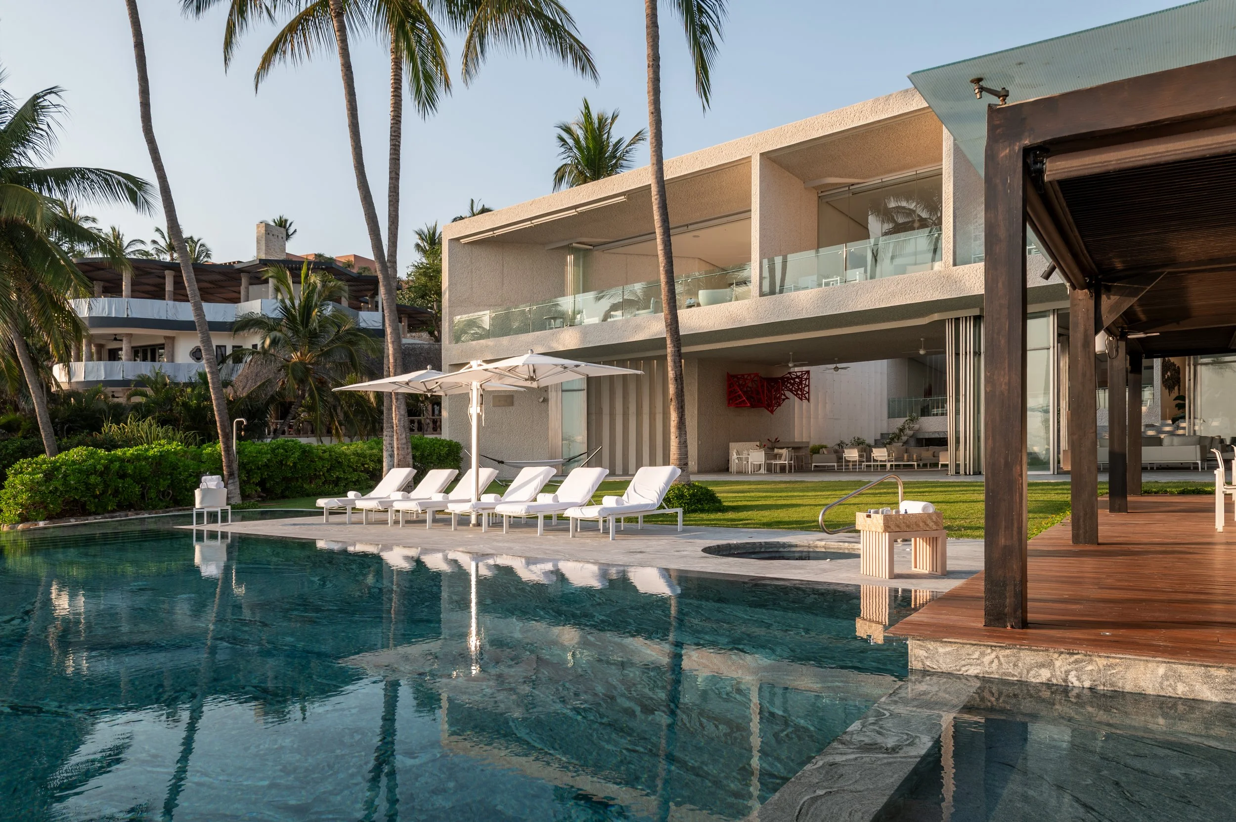 Luxury beachfront house with a swimming pool, palm trees, and outdoor lounge area.