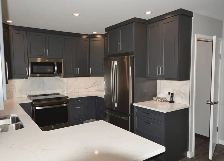 Modern kitchen with dark gray cabinets, stainless steel appliances, marble backsplash, and white countertops.