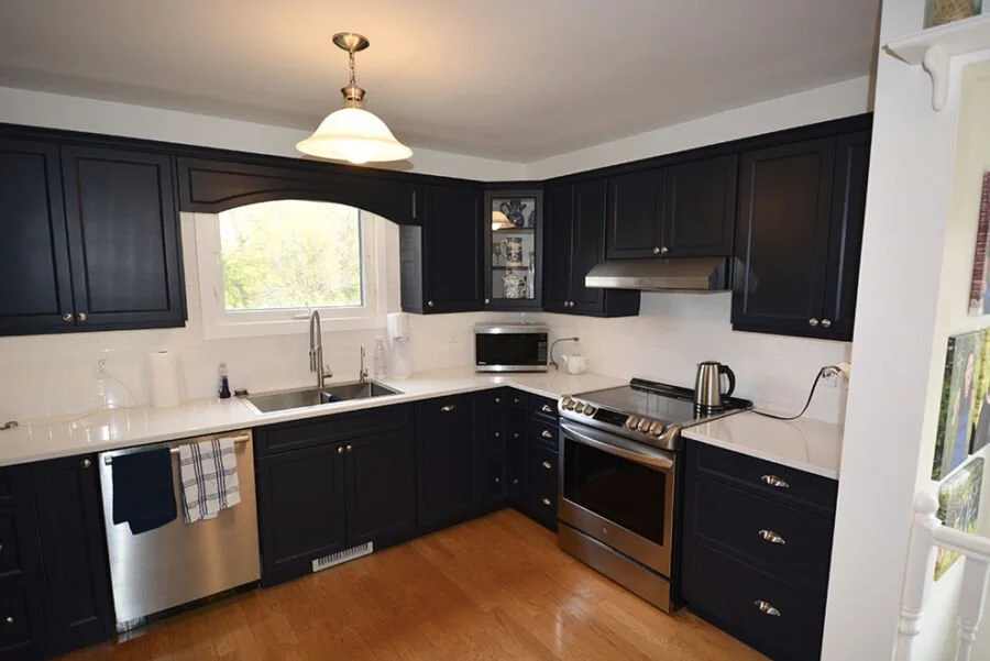 Kitchen with black cabinets, white countertops, stainless steel dishwasher and stove, microwave, kettle, and a window above the sink