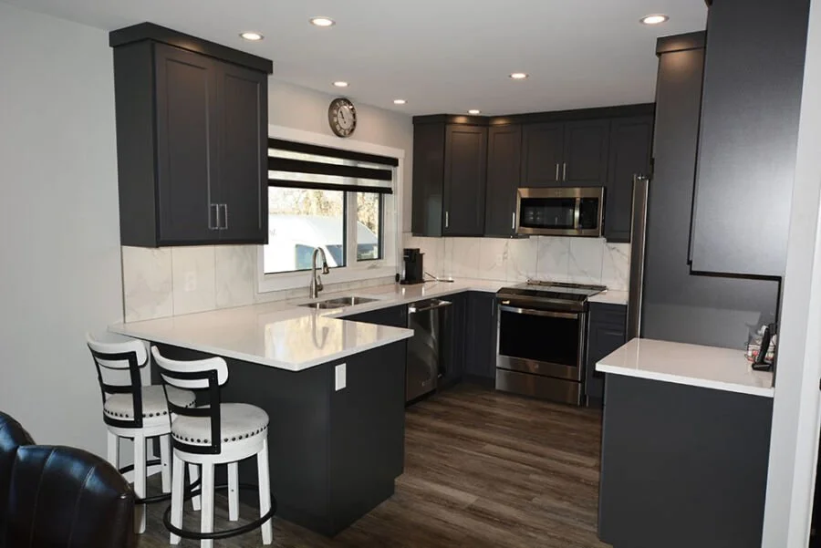 Modern kitchen with dark cabinets, white marble countertops, stainless steel appliances, and a window above the sink.