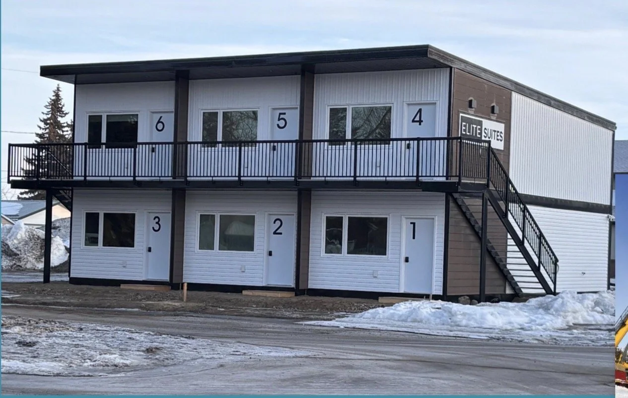 Two-story building with six separate units, numbered 1 through 6, with an external staircase on the right side leading to a balcony on the second floor. Sign reads 'Elite Suites,' indicating it is a motel or hotel. It is winter with snow on the ground.