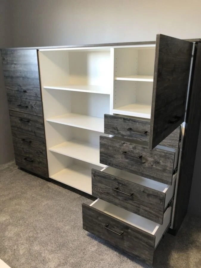 A large modular storage cabinet with dark wood trim and white shelves, featuring open and closed compartments, placed on a carpeted floor.