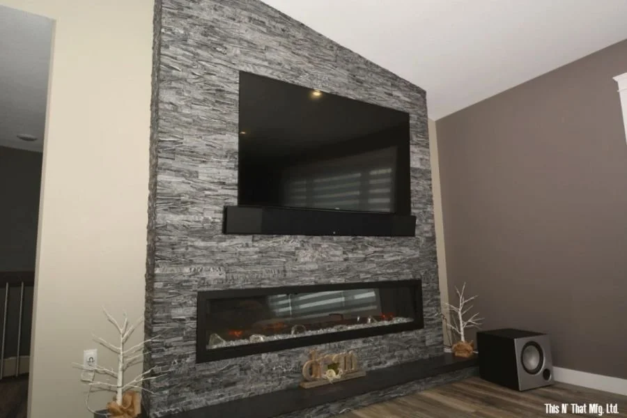 Living room with gray stone accent wall, mounted flat-screen TV, linear electric fireplace, decorative white leafless trees, and a speaker.