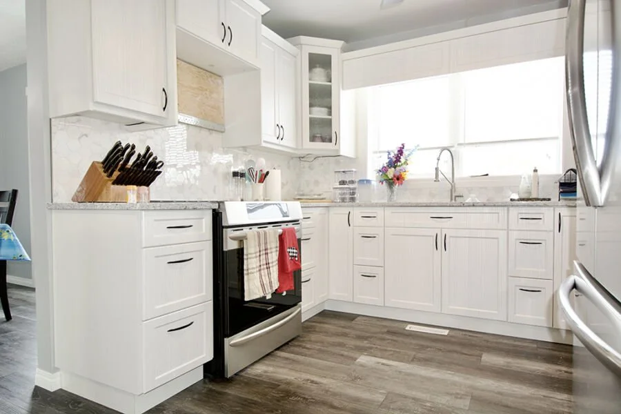 Bright white kitchen with cabinets, countertops, stove, and a large window with a vase of flowers.