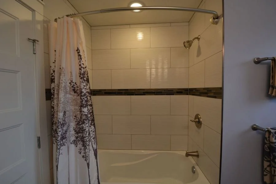 Bathroom shower with beige tile walls, a shower curtain, and a built-in bathtub.