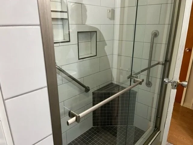 Shower with glass enclosure, built-in shelves, and grab bars, in a bathroom.