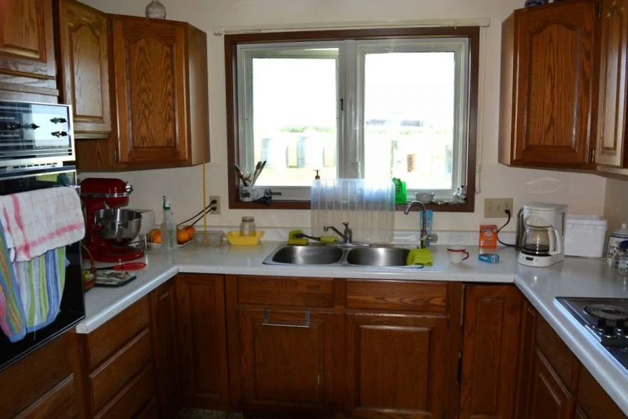 A kitchen with wooden cabinets, a window above the sink, and various kitchen appliances on the counter, including a coffee maker, stand mixer, and stove.
