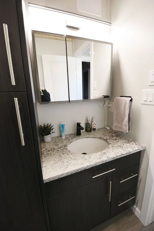 Bathroom vanity with granite countertop, oval sink, dark wood cabinets, mirror, small plant, toiletries, and towel.